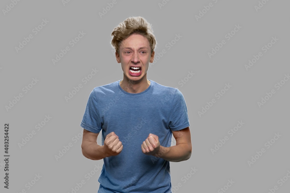 Angry stressed teen boy shouting on gray background. Emotional portrait of teen boy screaming with clenched fists. Angry stressed teen boy shouting on gray background. Emotional portrait of teen boy screaming with clenched fists.