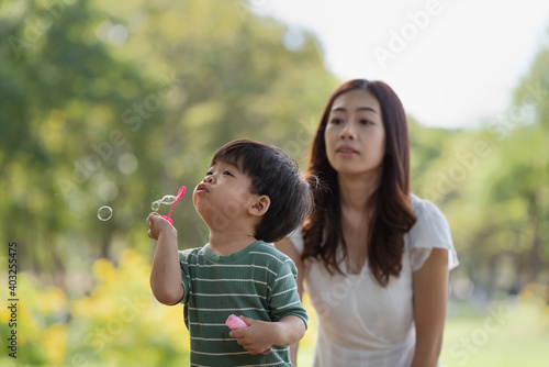 Asian family having fun mother and her son playing with soap bubbles in the park together