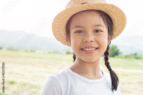 Beautiful asian little girl on the meadow in summer day. Happy little girl in a hat on a background of nature. Happy childhood concept.
