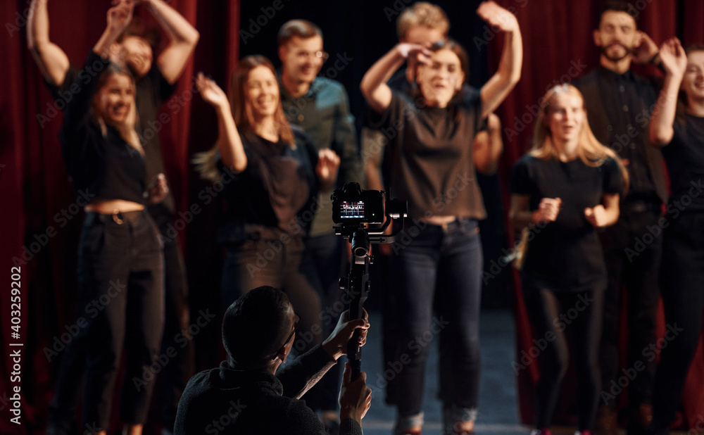 Happy people celebrating success. Group of actors in dark colored clothes on rehearsal in the theater