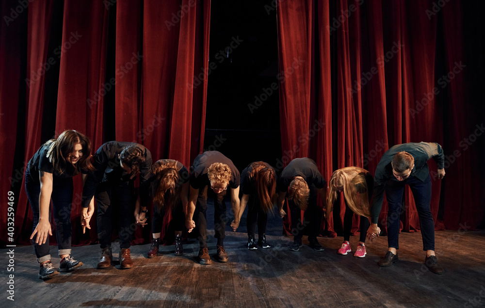 People bowing to audience. Group of actors in dark colored clothes on rehearsal in the theater - obrazy, fototapety, plakaty 