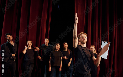 Man with notepad practice his role. Group of actors in dark colored clothes on rehearsal in the theater