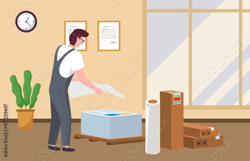 Male worker in a printing studio near boxes and rolls. Man in uniform holds a stack of large sheets of paper. Employee of a printing house at work prepares paper for a printing machine or plotter