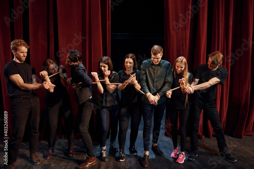 With rope in hands. Group of actors in dark colored clothes on rehearsal in the theater