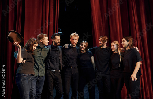 Standing against red curtains. Group of actors in dark colored clothes on rehearsal in the theater