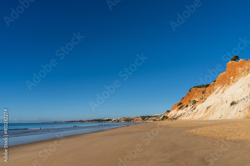 view of a wide empty golden sand beach with colorful sand cliffs on a sunny day