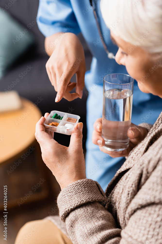 nurse pointing at pills in hand of senior woman with glass of water, blurred background nurse pointing at pills in hand of senior woman with glass of water, blurred background