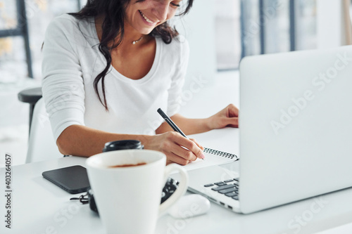 Using laptop and notepad. Young female freelancer working indoors in the office at daytime