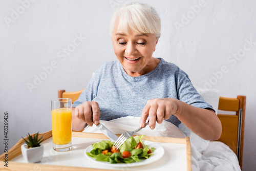 pleased senior woman having breakfast in bed on blurred foreground