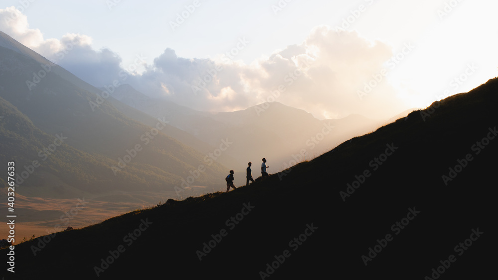 Silhouette of three men climbing a mountain at sunset 
