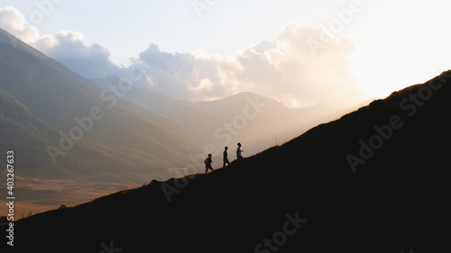 Silhouette of three men climbing a mountain at sunset 