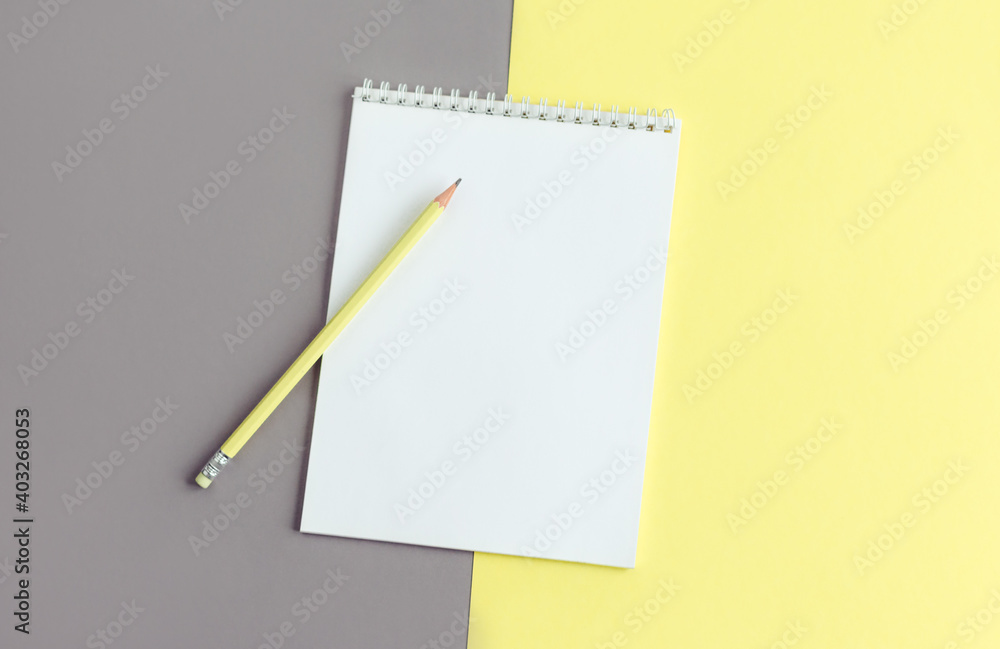 Notebook with blank page and pencil on a yellow and grey background. Notebook with blank page and pencil on a yellow and grey background.