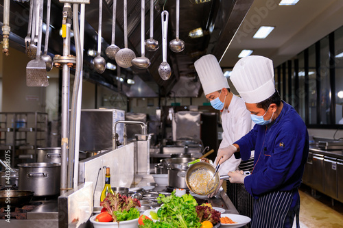 Asian male chef cooking food with his colleuge in the hotel kitchen