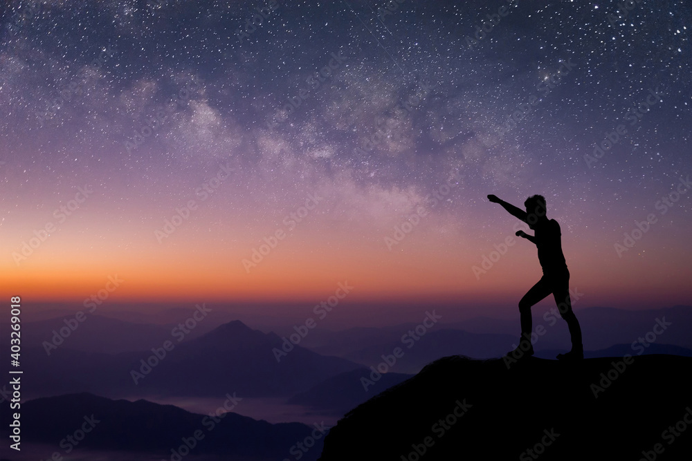 Silhouette of young traveler standing and open arms and watched the star and milky way on top of the mountain before sunrise. He is happy to be with herself and stay with nature at twilight time.