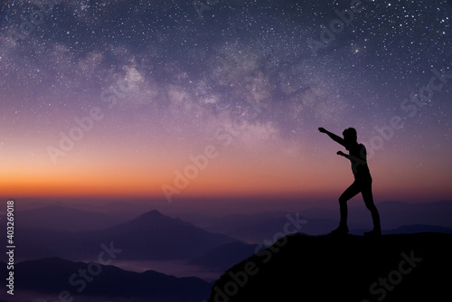 Silhouette of young traveler standing and open arms and watched the star and milky way on top of the mountain before sunrise. He is happy to be with herself and stay with nature at twilight time.