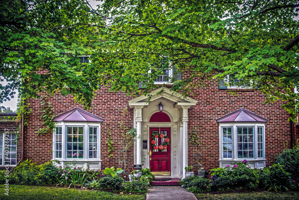 Traditional brick house with bay windows and pillars in summer with landscaping and door wreath and No soliciting sign and large maple trees