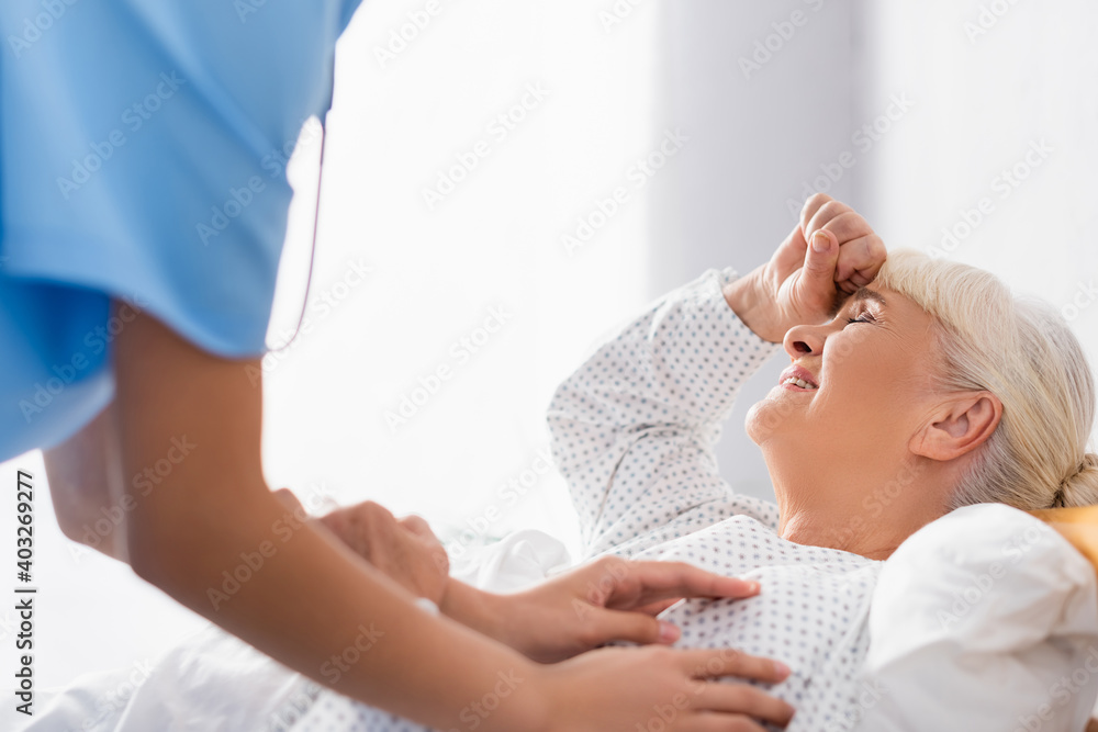 Obraz premium nurse touching elderly woman suffering from headache while lying with closed eyes, blurred foreground