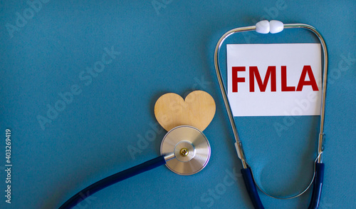 FMLA symbol. White card with word 'FMLA - family medical leave act' and stethoscope on blue background. Wooden heart. Medical and FMLA - family medical leave act concept, copy space. photo
