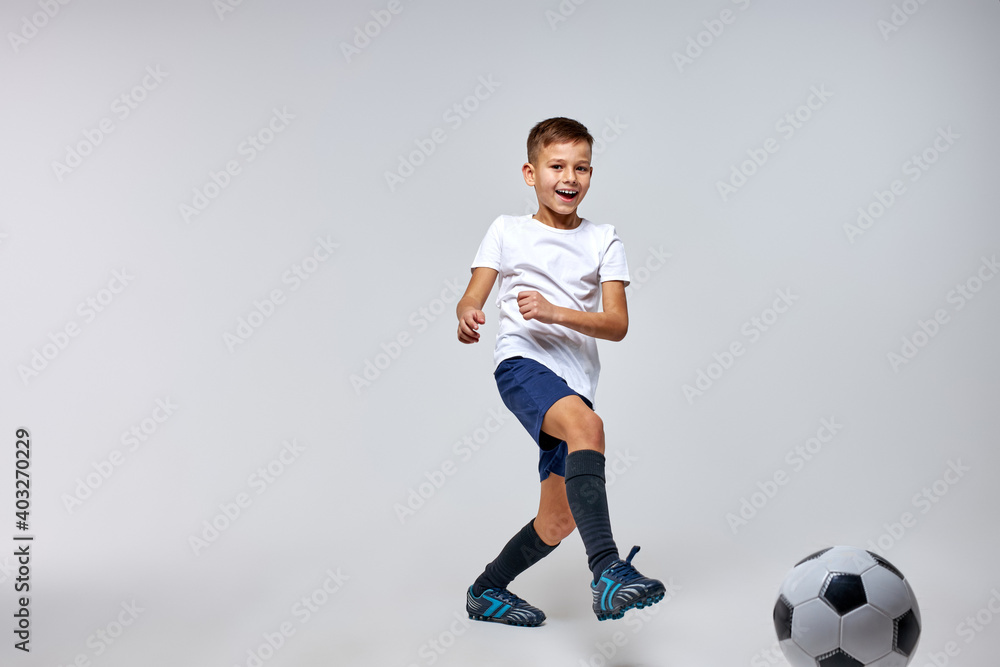 boy soccer player playing with ball, kicking it, training before match. isolated in studio, wearing uniform