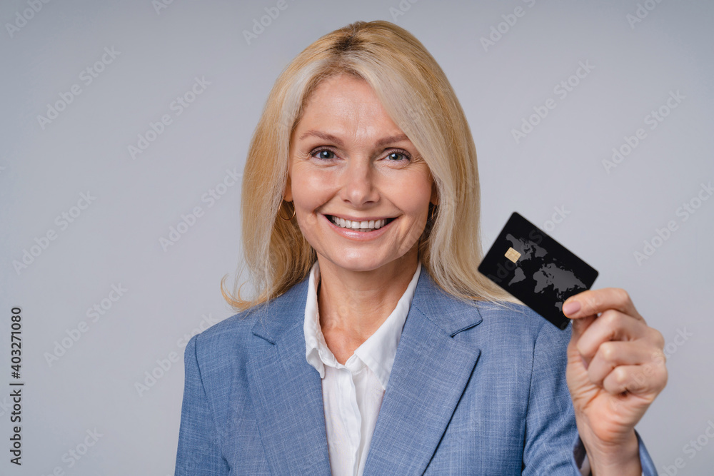 Confident middle-aged business woman with credit card isolated over grey background Confident middle-aged business woman with credit card isolated over grey background