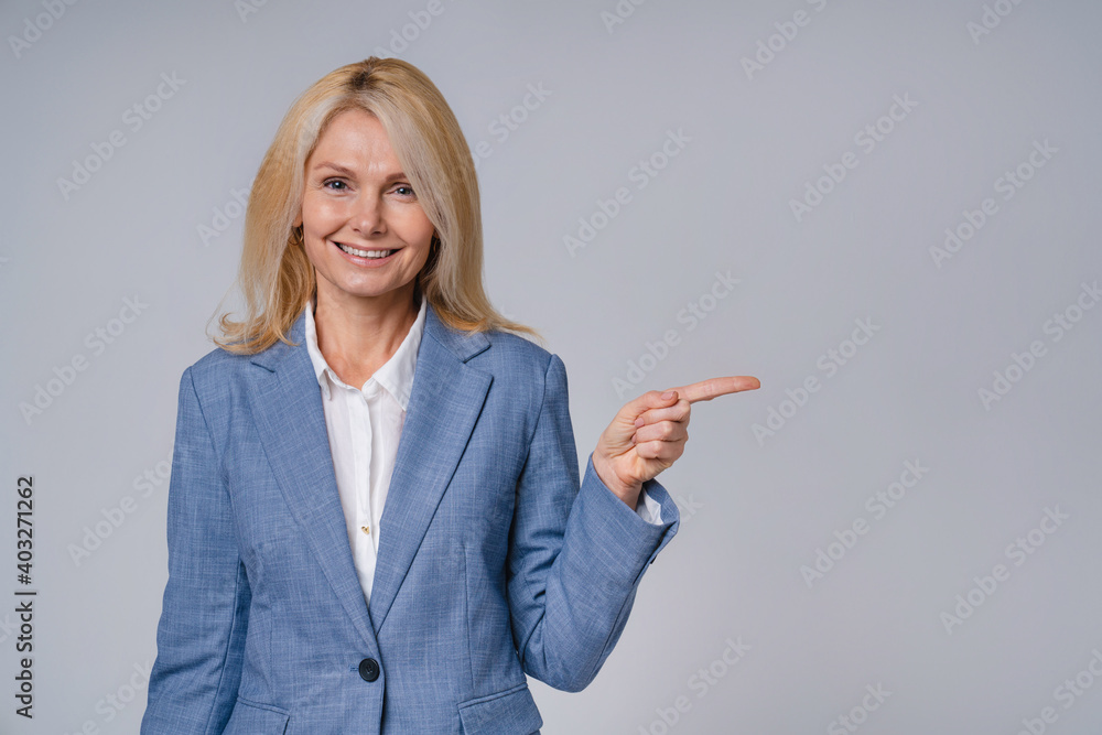 Happy senior business woman pointing at copy space isolated over grey background Happy senior business woman pointing at copy space isolated over grey background