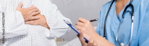 cropped view of senior woman touching chest while suffering from gasp attack near nurse writing on clipboard, blurred foreground, banner