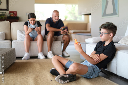 Componenti di una Famiglia seduti nel salotto di casa si auto isolano con giochi elettronici, cellulare e tablet © alex.pin