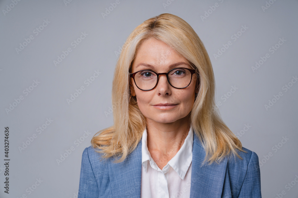 Smart confident successful senior business woman in glasses and formal outfit isolated over grey background