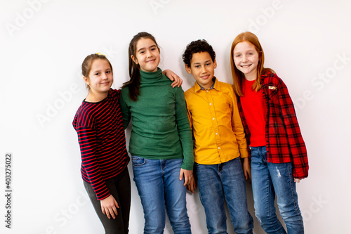 Portrait of cute little kids in jeans looking at camera and smiling, standing against white wall