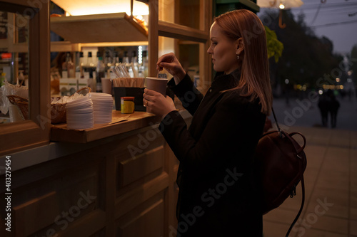 Beautiful Caucasian female is ordering delicious coffee to go at street cafe outdoors in the evening