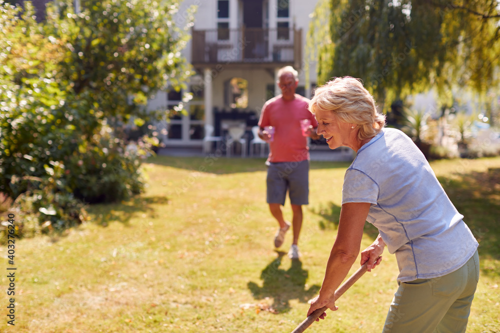Retired Man Bringing Cold Drink To Woman Tidying Garden With Rake Retired Man Bringing Cold Drink To Woman Tidying Garden With Rake