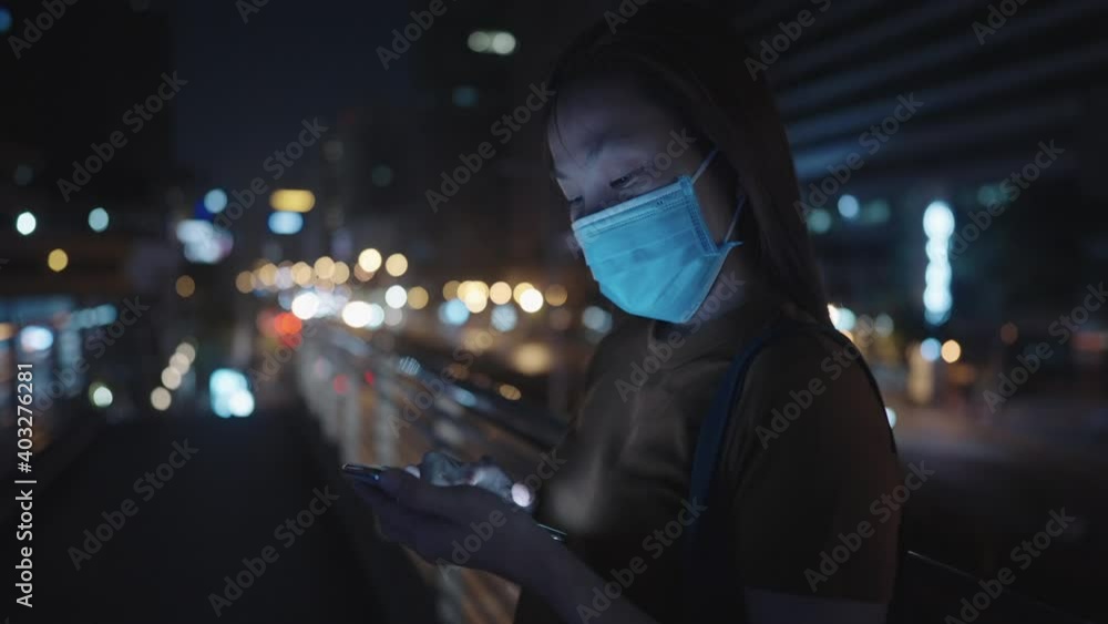 slow motion close up woman wearing medical face mask and reading app in mobile phone in downtown city at night have traffic street light as background slow motion close up woman wearing medical face mask and reading app in mobile phone in downtown city at night have traffic street light as background