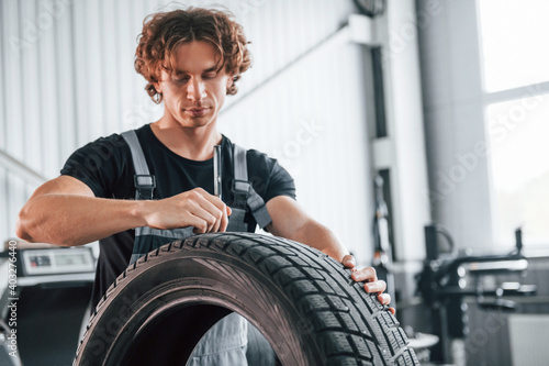 Fixes broken tire. Adult man in grey colored uniform works in the automobile salon