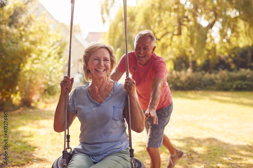 Retired Couple Having Fun With Man Pushing Woman On Garden Swing