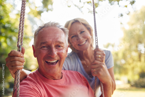 Portrait Of Retired Couple Having Fun With Woman Pushing Man On Garden Swing