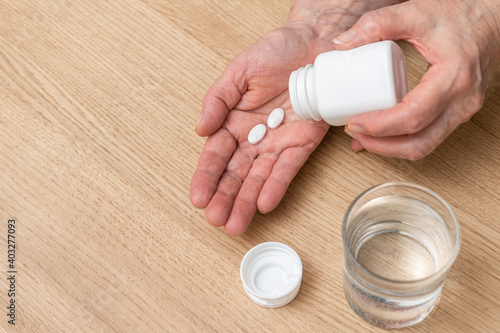 White pills of painkiller or antibiotic for treatment on senior woman hand palm, glass with water, medicines and vitamin supplements concept,close-up view