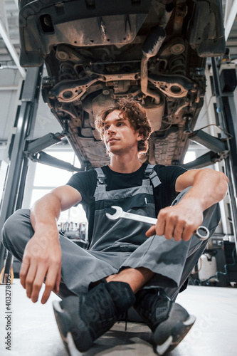 Handsome adult man in grey colored uniform sits below automobile