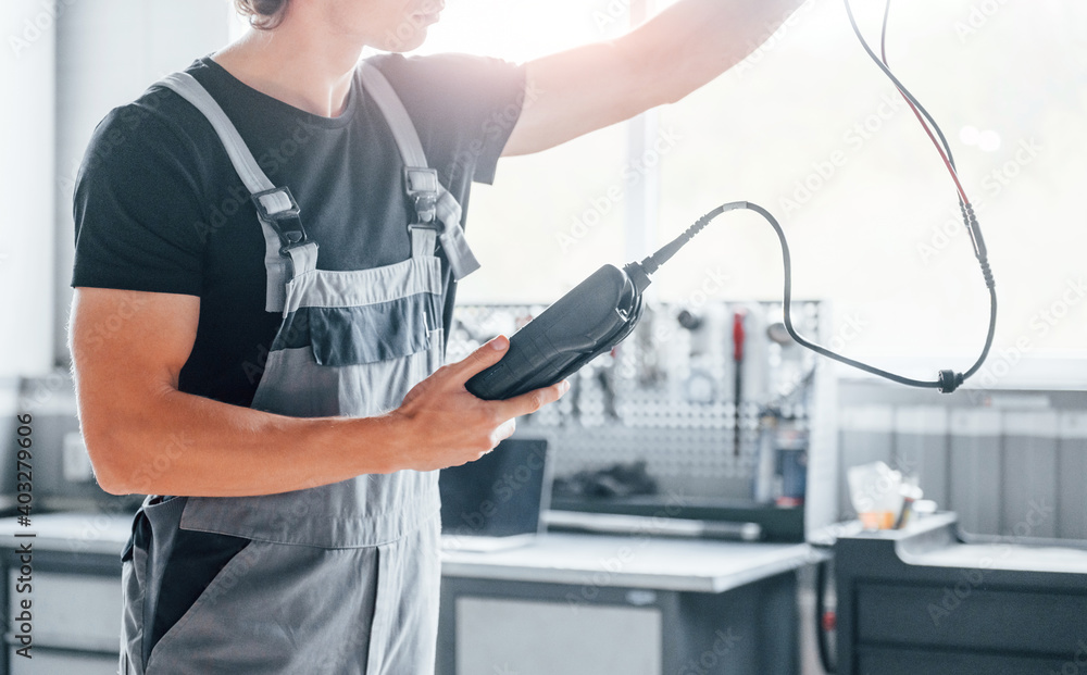 Special tool for testing characteristics. Adult man in grey colored uniform works in the automobile salon