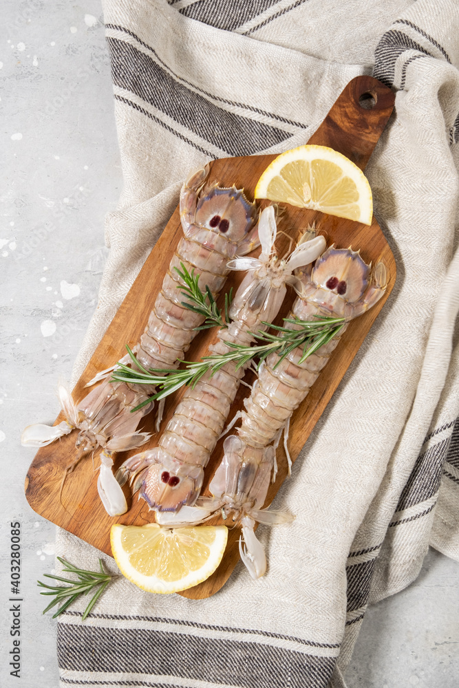 Fresh raw seafood large mantis shrimps with lemon on a gray concrete background. ingredients in a store or seafood restaurant , background for a fish menu