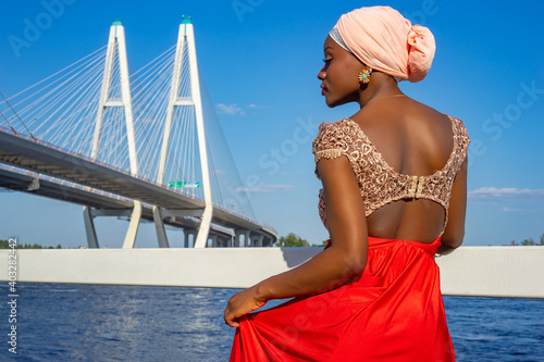 Dark-skinned model near the cable-Stayed bridge. African-American woman walks around Petersburg on summer day. Dark-skinned girl is standing with her back turned, her face turned in profile. photo