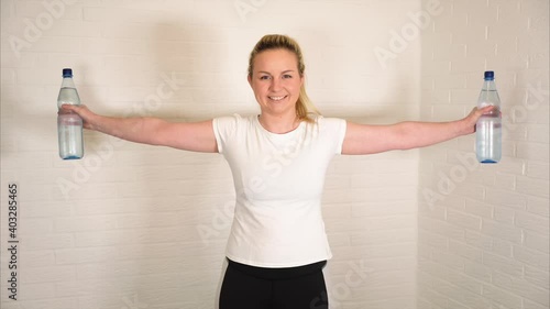 Happy blonde woman doing fitness exercise with water bottles - basic sport workout as a training at home photo