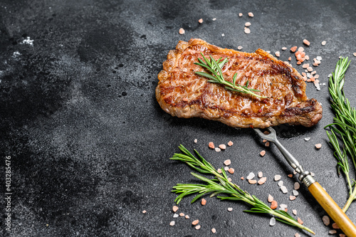 Grilled Striploin steak or strip new York on a meat fork. Black background. Top view. Copy space