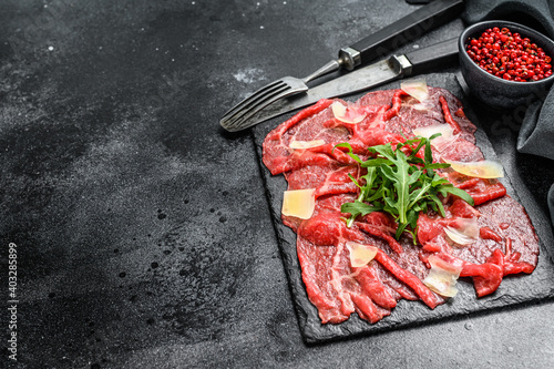 Beef carpaccio on black plate with parmesan cheese and arugula. Black background. Top view. Copy space.