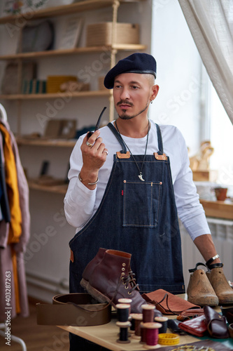 craftsman relax at work place, holding smoking pipe in mouth. man in apron have rest in workshop