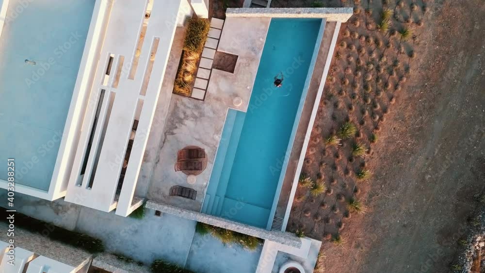 Woman swimming alone in a pool outside a modern villa aerial