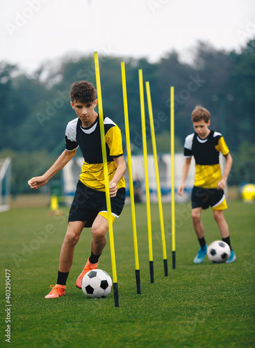 Young Football Players Running Slalom and Dribbling With Balls Between Training Poles. Soccer Practice for Teenage Boys. Junior Level Soccer Team Traing Unit