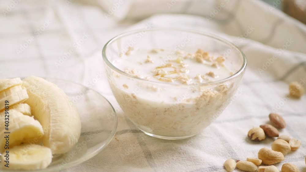 Overnight oatmeal bowl. Cooking healthy breakfast at home. Plant milk pouring. Banana, honey, and nuts ingredients. 4k video. Step by step recipe Overnight oatmeal bowl. Cooking healthy breakfast at home. Plant milk pouring. Banana, honey, and nuts ingredients. 4k video. Step by step recipe