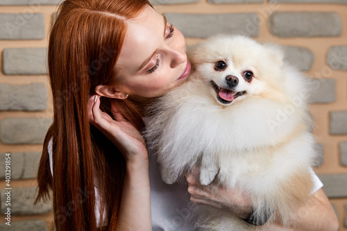 female in love of her fluffy spitz after grooming procedure, she is hugging her pet and smiling
