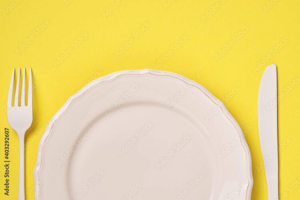 White plate, fork and spoon on a trendy yellow background. Time to eat. Diet concept. Top view. White plate, fork and spoon on a trendy yellow background. Time to eat. Diet concept. Top view.