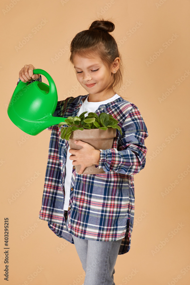 Little girl watering plants in a flower pot on beige studio background. the child dreams of becoming a gardener Little girl watering plants in a flower pot on beige studio background. the child dreams of becoming a gardener
